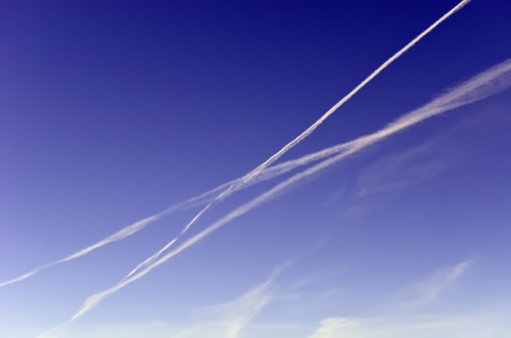Travel concept of intersecting journeys Three contrails crisscrossing while another dissipates across blue sky.jpeg